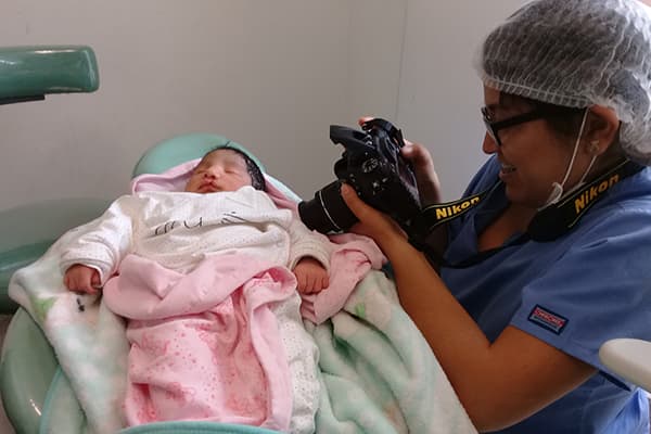 A nurse taking a photo of a baby girl with a cleft palate. wrapped in pink