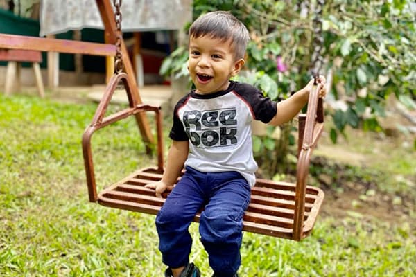 A young latino boy with a Reebok t-shirt sitting on a garden swing and smiling at the camera