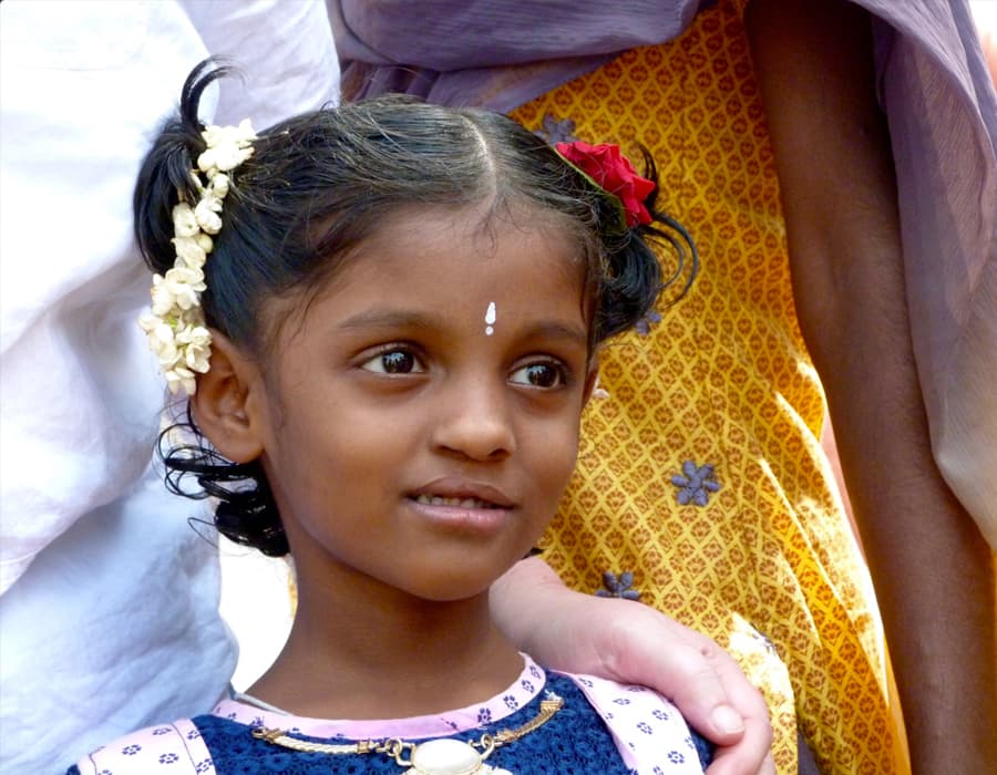 Close up of child looking outward, with her parents hand on her shoulder.