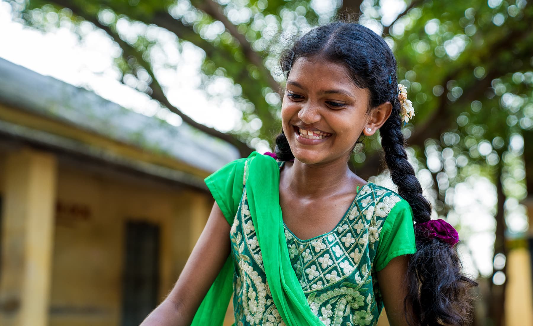 A smiling child looks downward while wearing a green saree